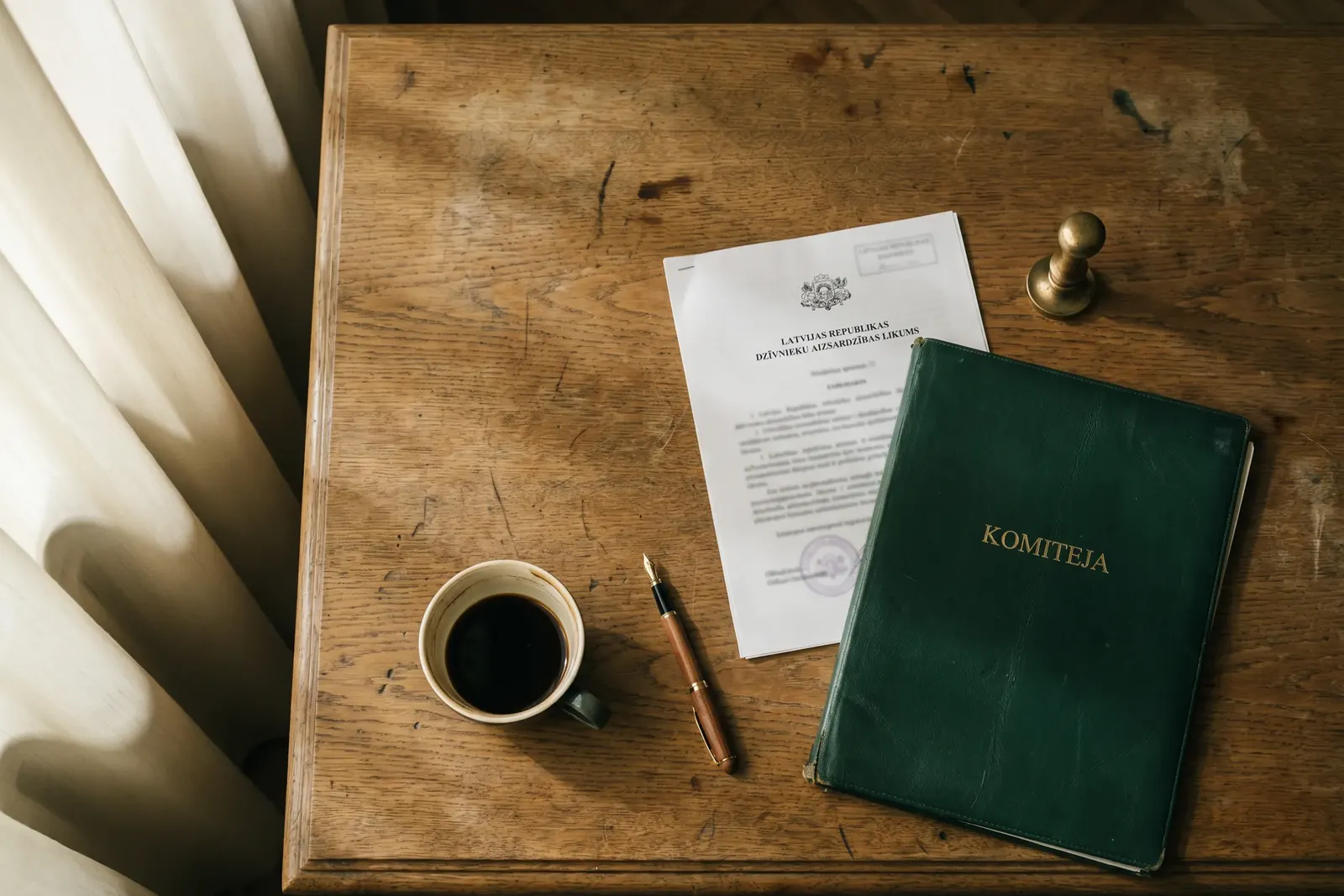 Photo from the ALHALAL website: a green folder marked KOMITEJA, a document, a pen, a stamp and a cup of coffee on a wooden desk